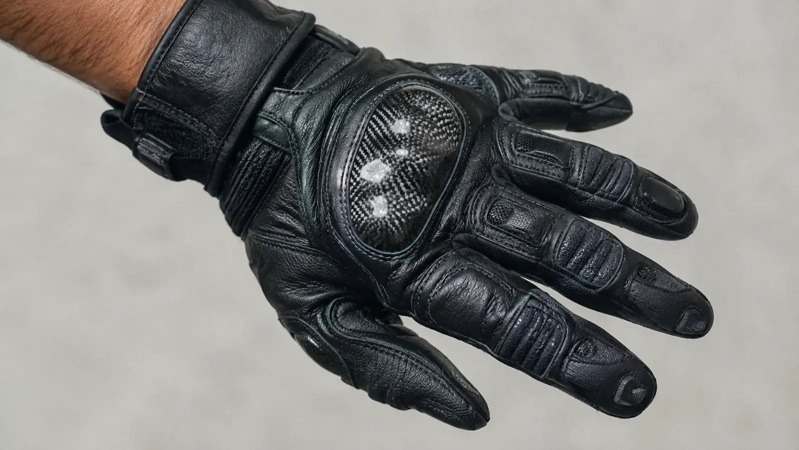 A close-up of a rider's hand in a leather motorcycle glove showing the knuckle armor and palm stitching