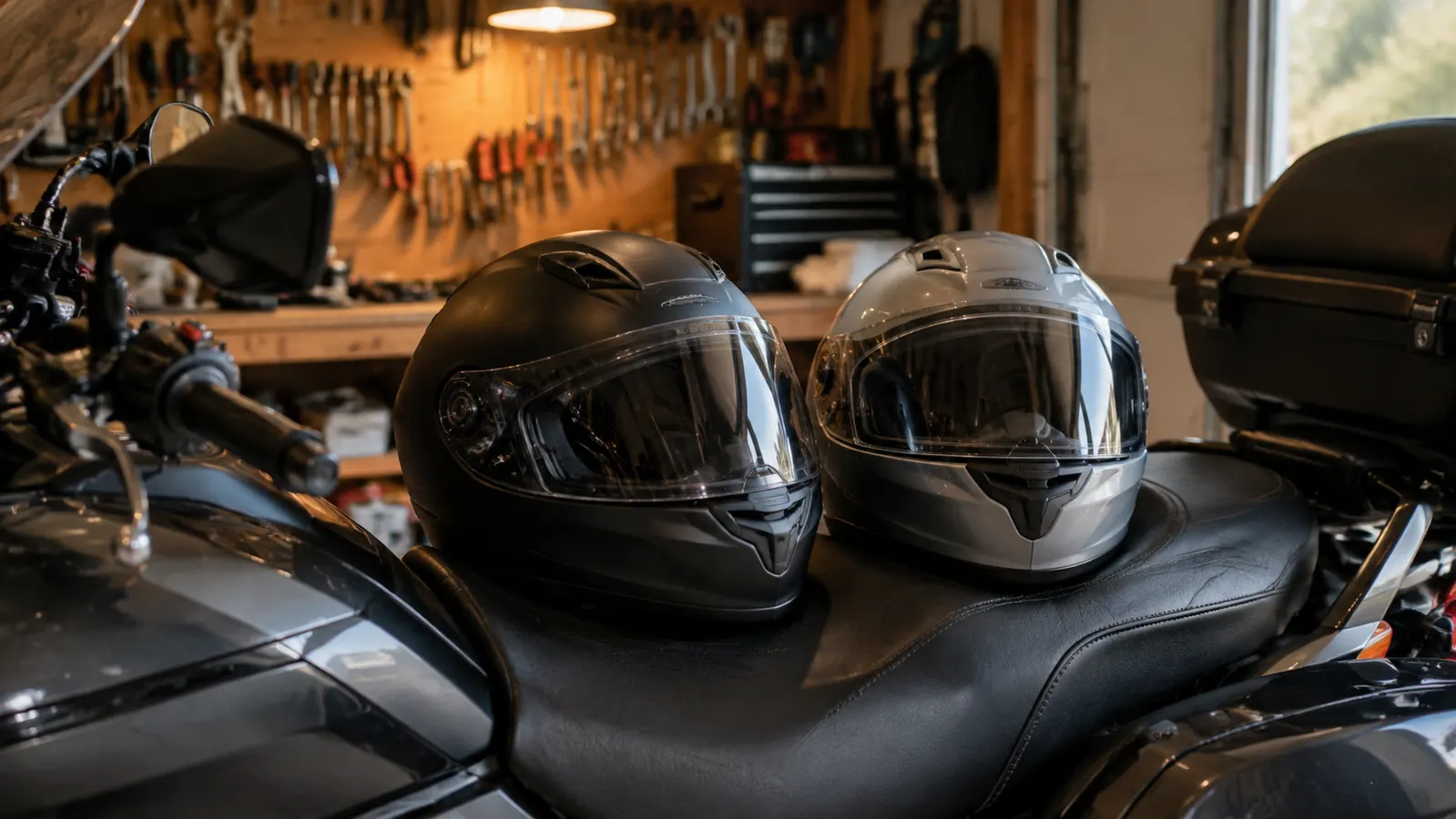 Two full-face motorcycle helmets side by side on the seat of a touring motorcycle in a garage.