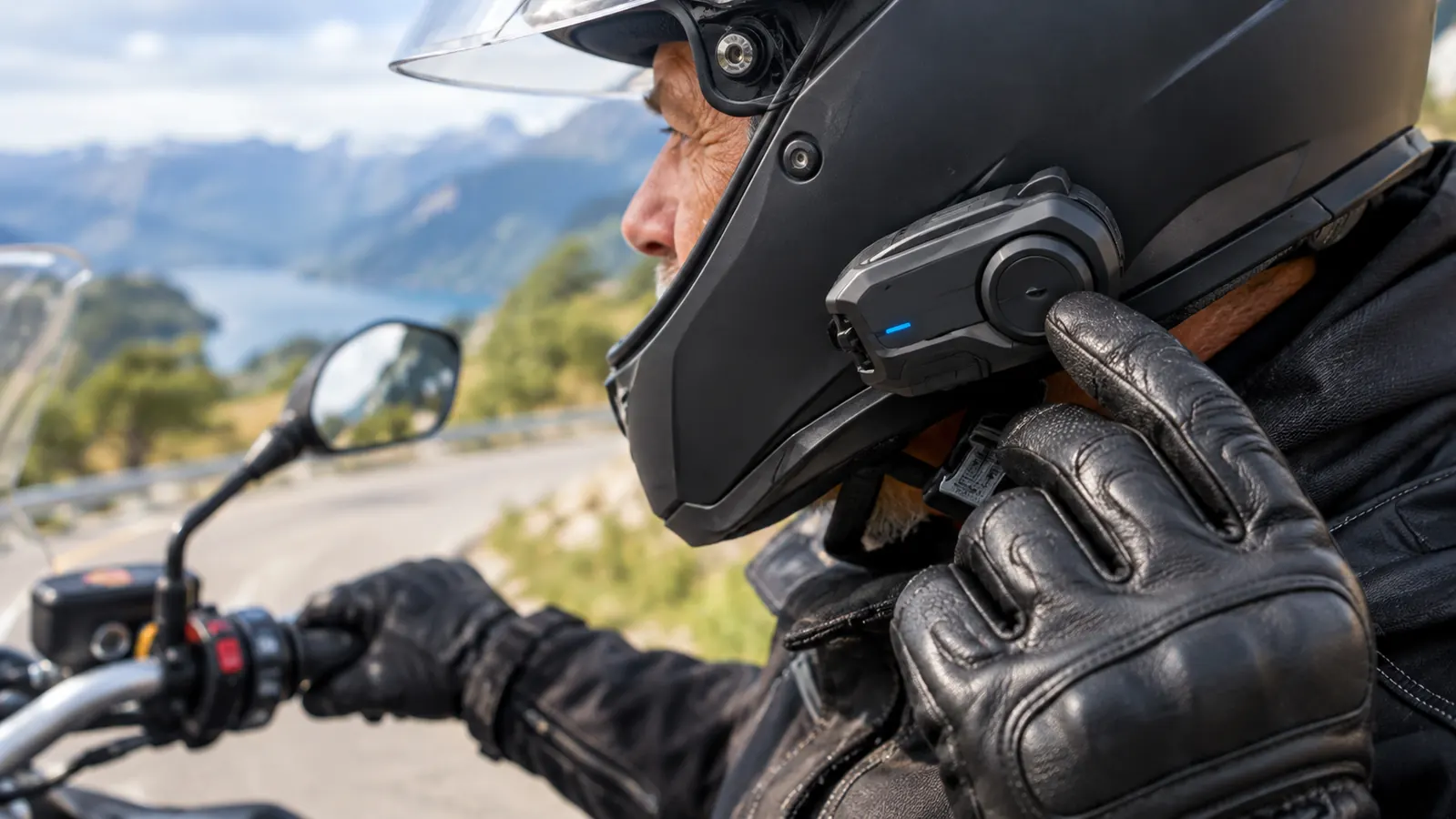 A rider's gloved hand reaching up to adjust a communicator mounted on the side of a helmet
