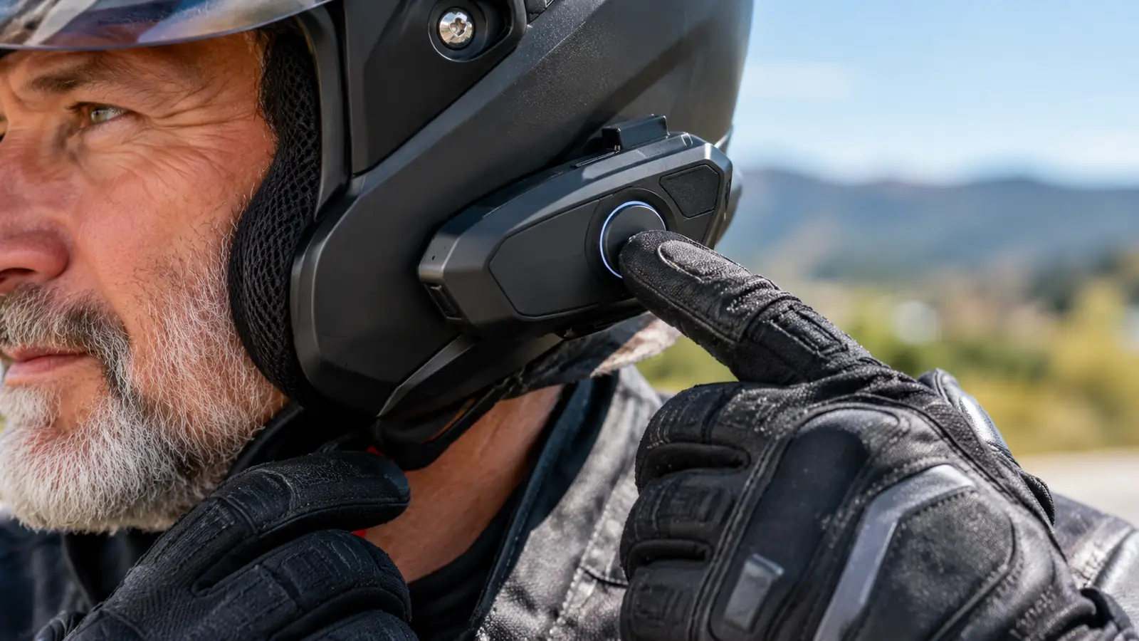 A rider's gloved hand pressing a button on the communication unit mounted to the side of a helmet