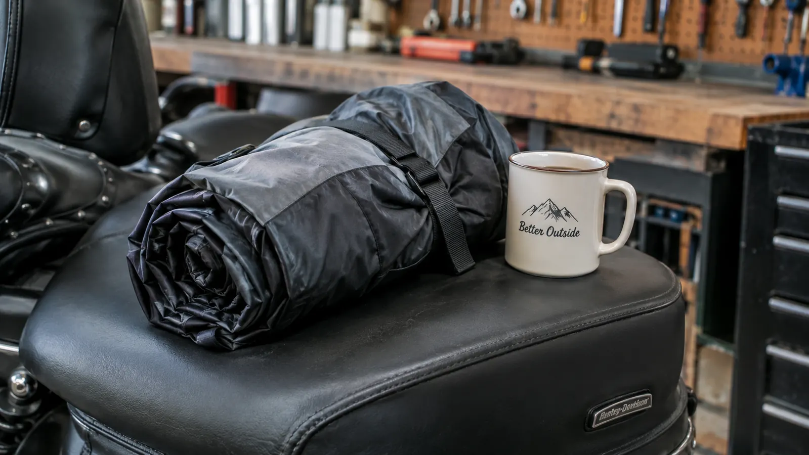 A rain suit jacket and pants folded into a compact roll on top of a saddlebag, coffee mug beside it for scale